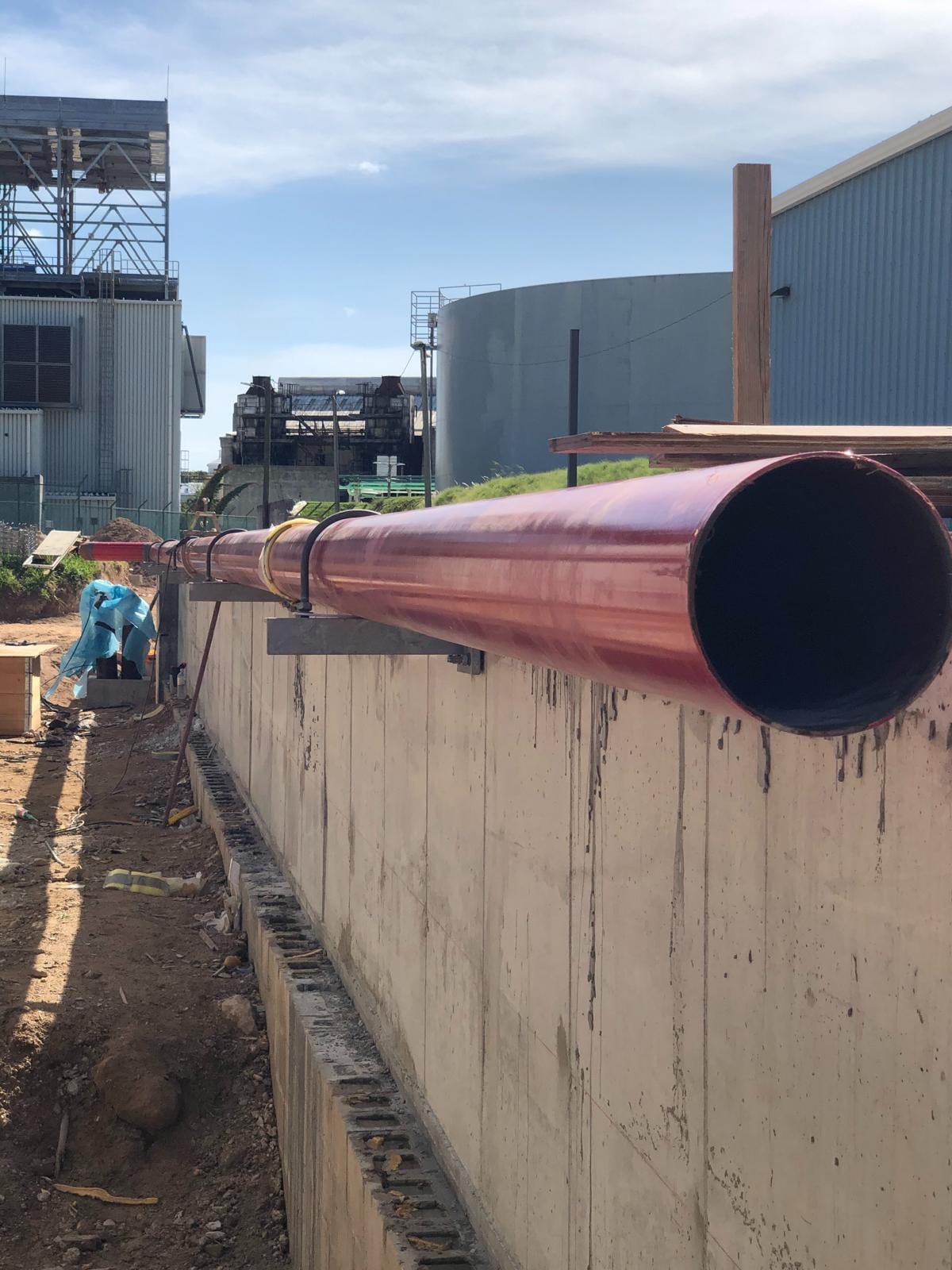 A long red-coated fire main running along a concrete wall on the BELCO power station site in Bermuda