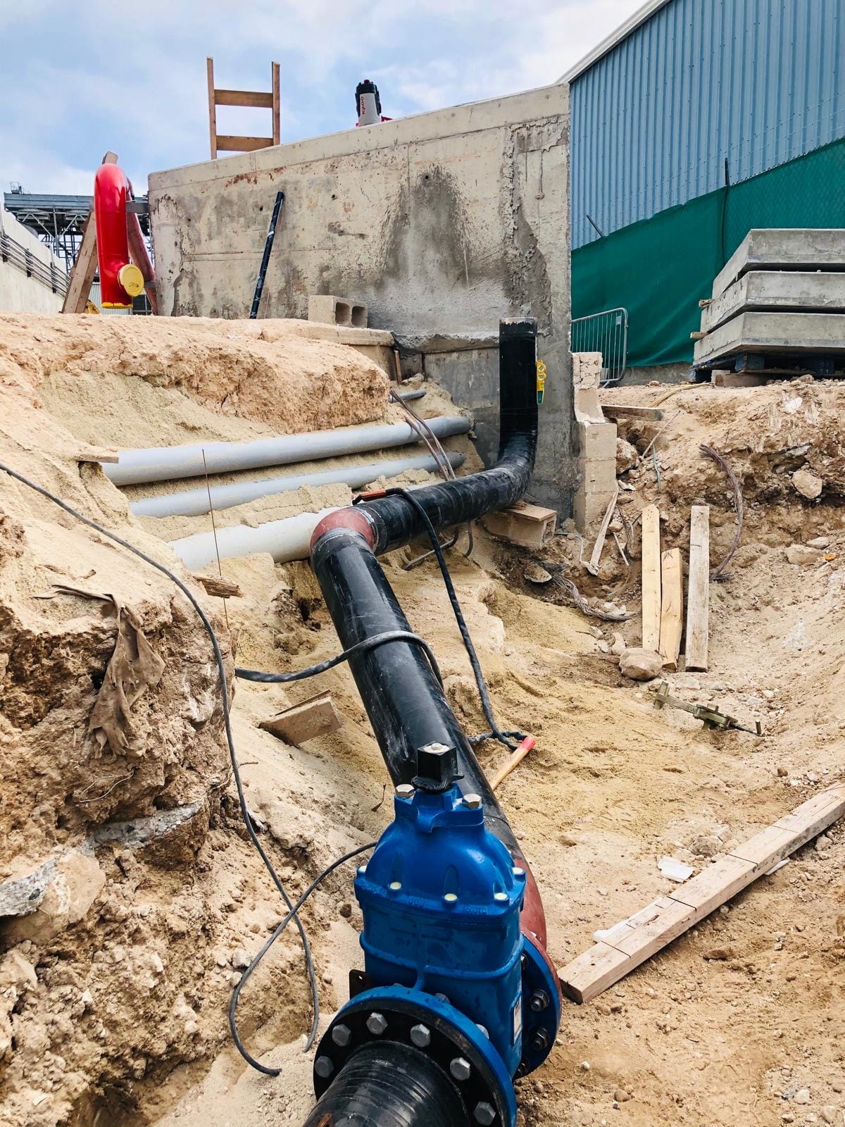 Blue gate valve flanged into the black-coated buried main in an open trench