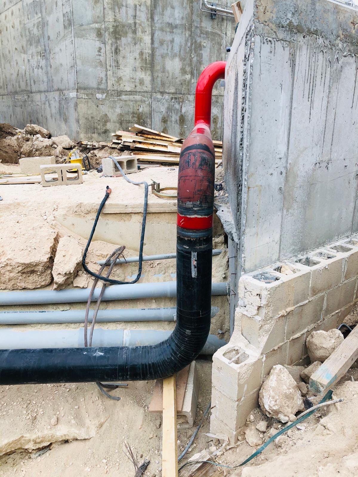 Red fire riser turning down into a black buried pipe against a concrete wall