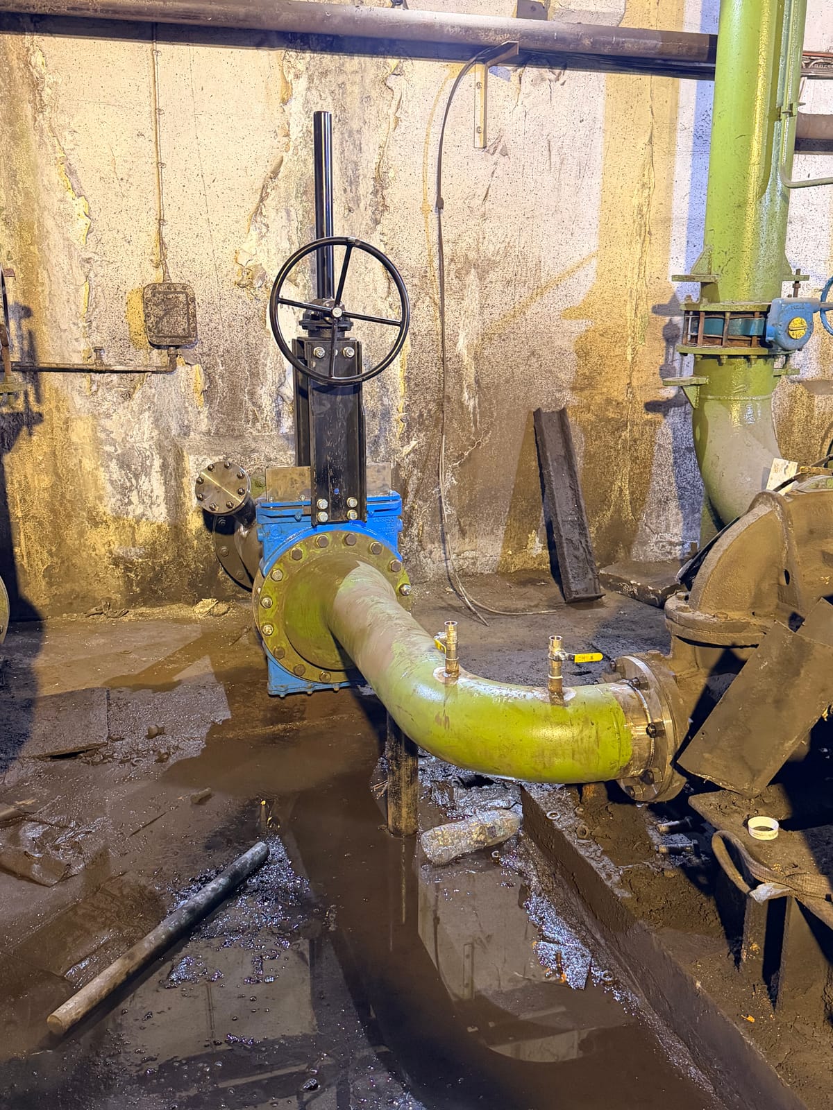 Blue knife gate valve and handwheel on new pipework against the chamber wall